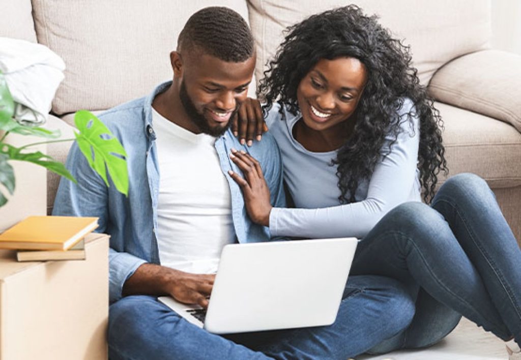 Casal negro sorrindo em frente ao notebook